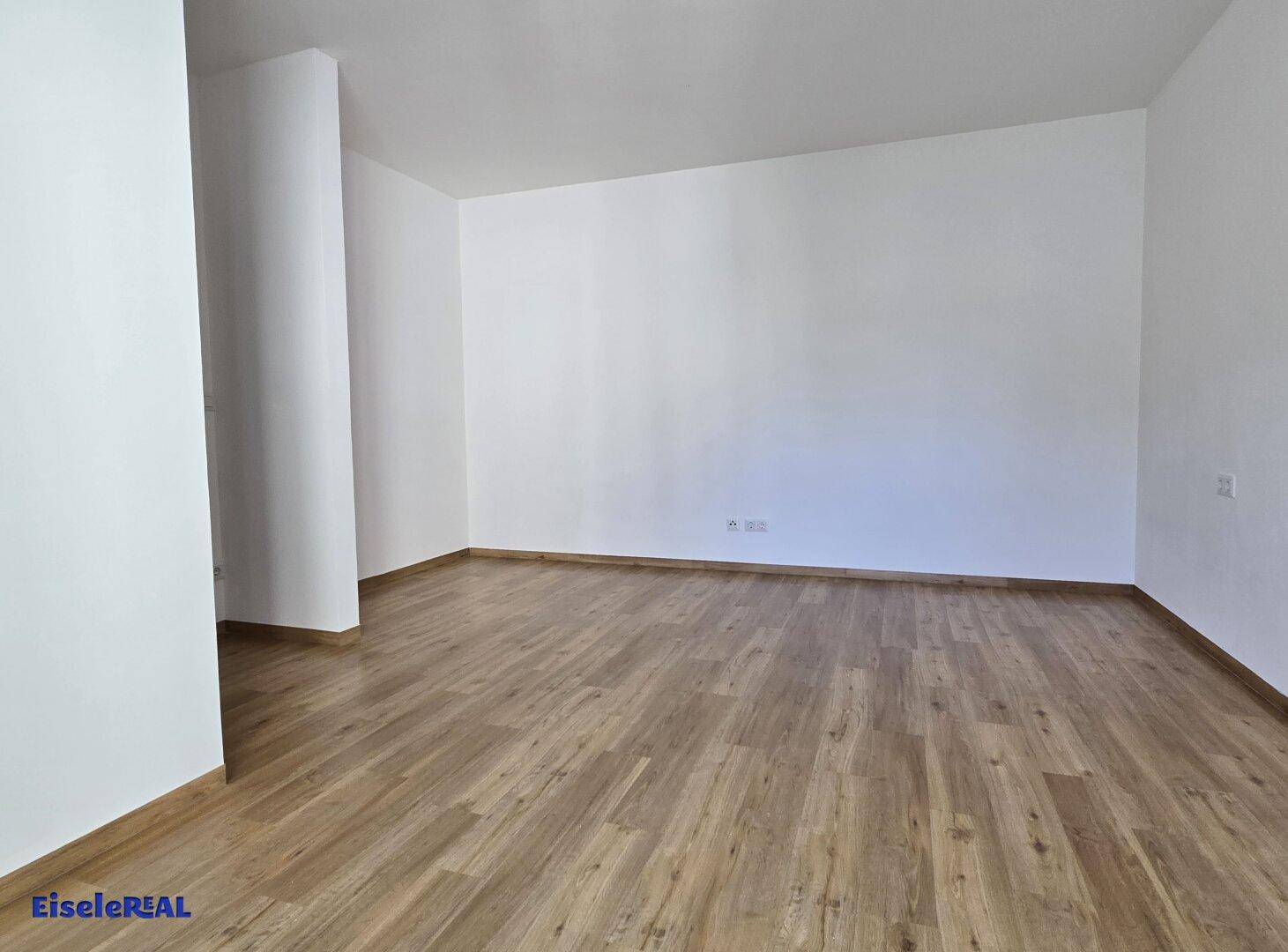 Geräumiger, leerer Raum mit hellem Laminatboden und weißen Wänden, bietet viel Gestaltungspotenzial.