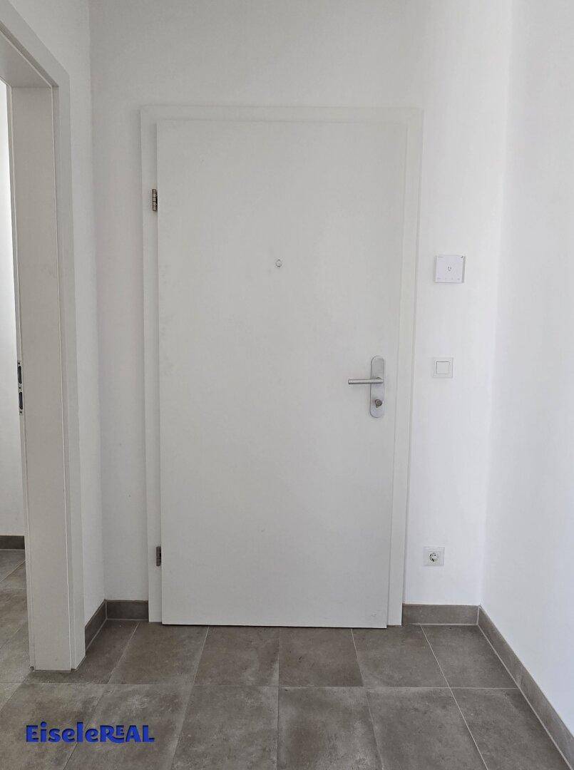 Weiße Eingangstür mit modernem Griff und gefliestem Boden im Flurbereich der Wohnung.