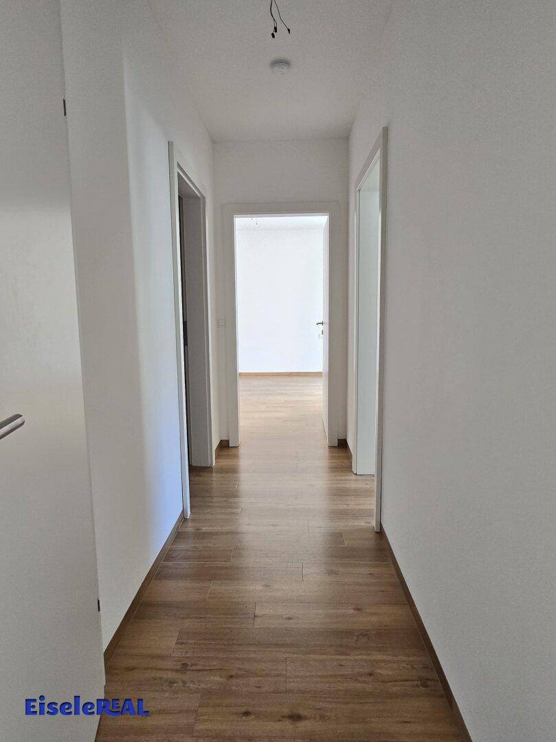 Langer, heller Flur mit Laminatboden, der zu den verschiedenen Zimmern der Wohnung führt.