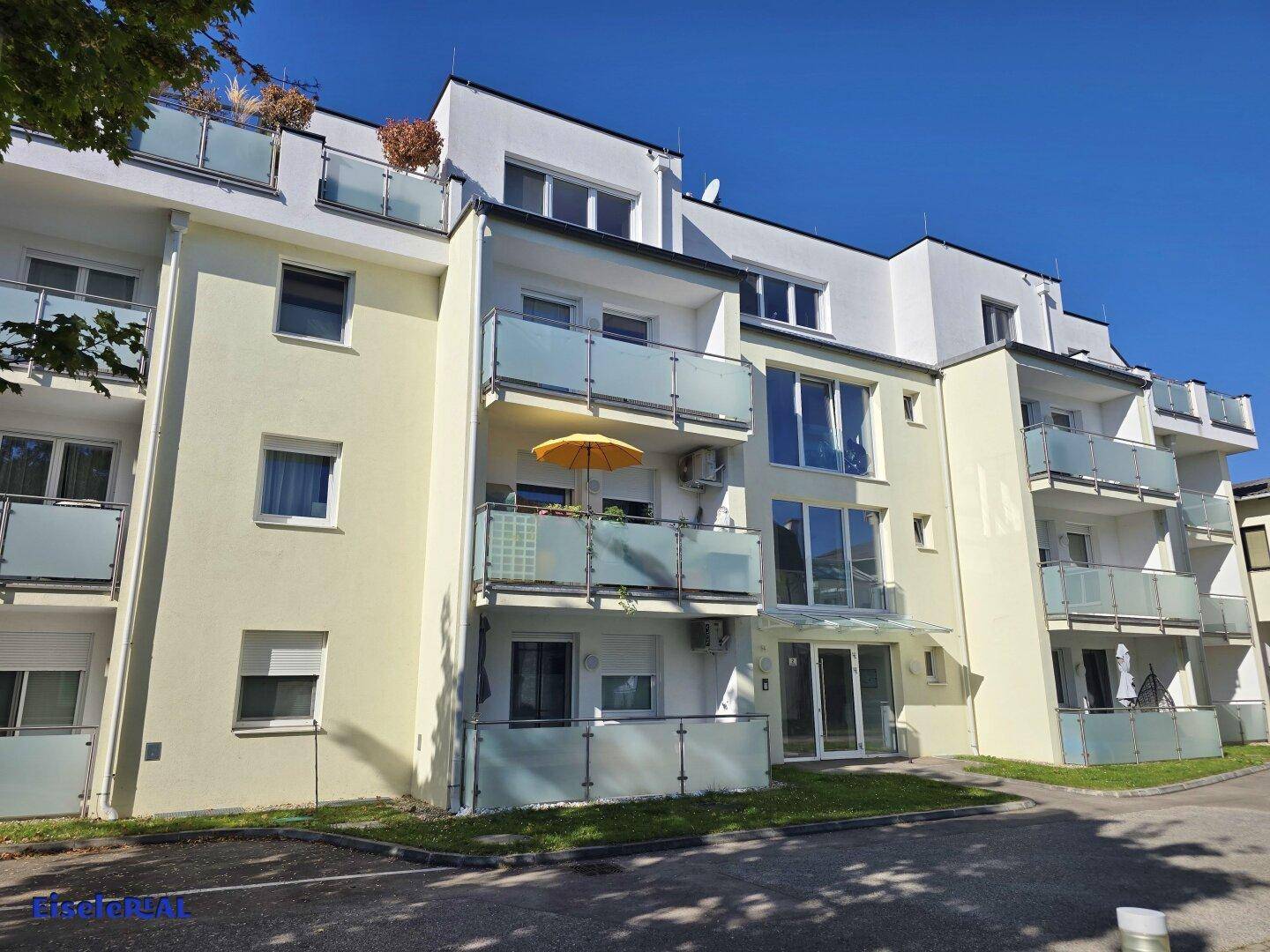 Modernes Wohngebäude mit hellgelber Fassade, vielen Balkonen und großen Fenstern unter blauem Himmel.