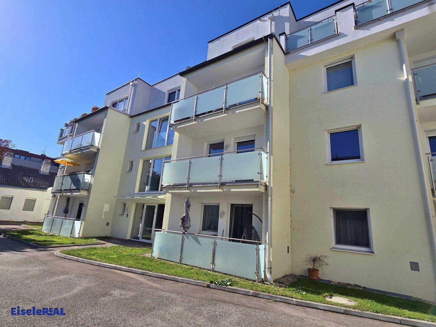 Ansicht des modernen Mehrfamilienhauses mit Balkonen und Glasgeländern unter strahlend blauem Himmel.