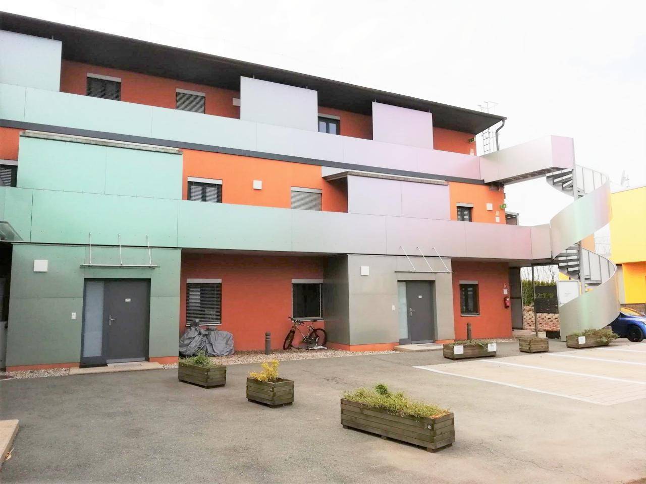 Moderne Wohnanlage mit farbiger Fassade, Außentreppe und Parkplätzen im Vordergrund.