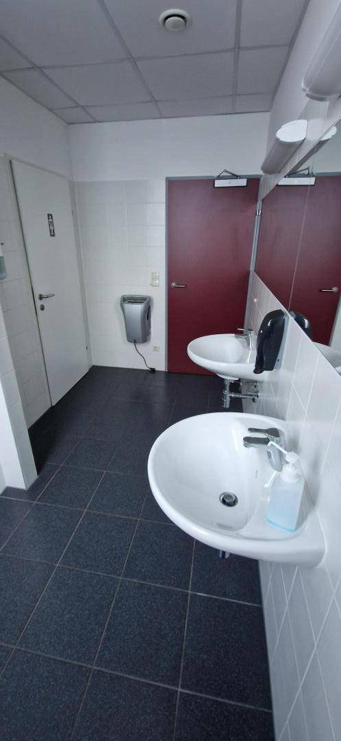 Waschraum mit mehreren Waschbecken, Spiegeln und dunklem Fliesenboden.