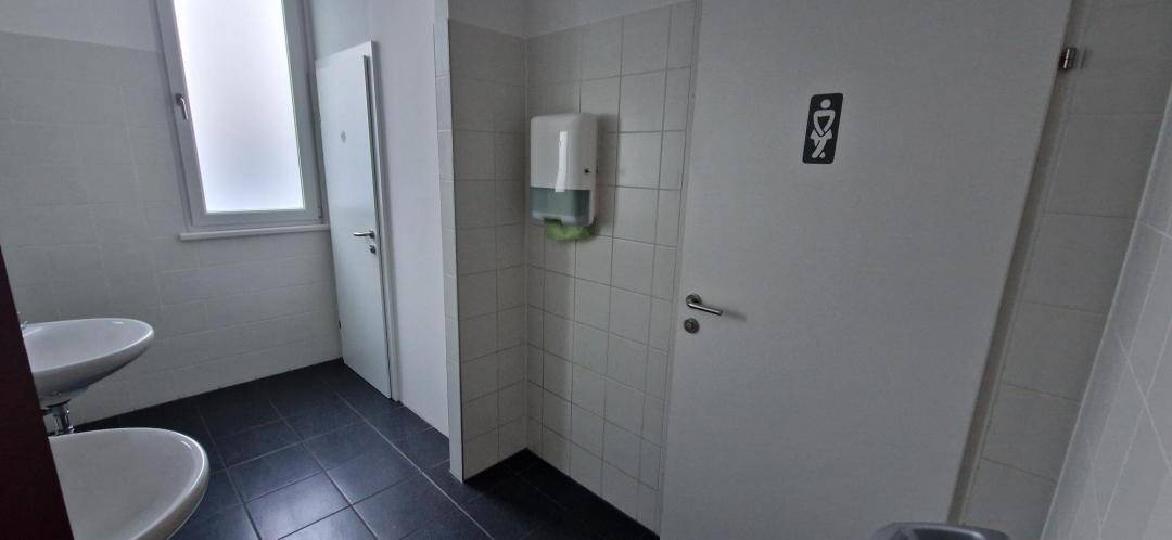 Toilettenraum mit zwei Waschbecken, weißen Fliesen und dunklem Boden.