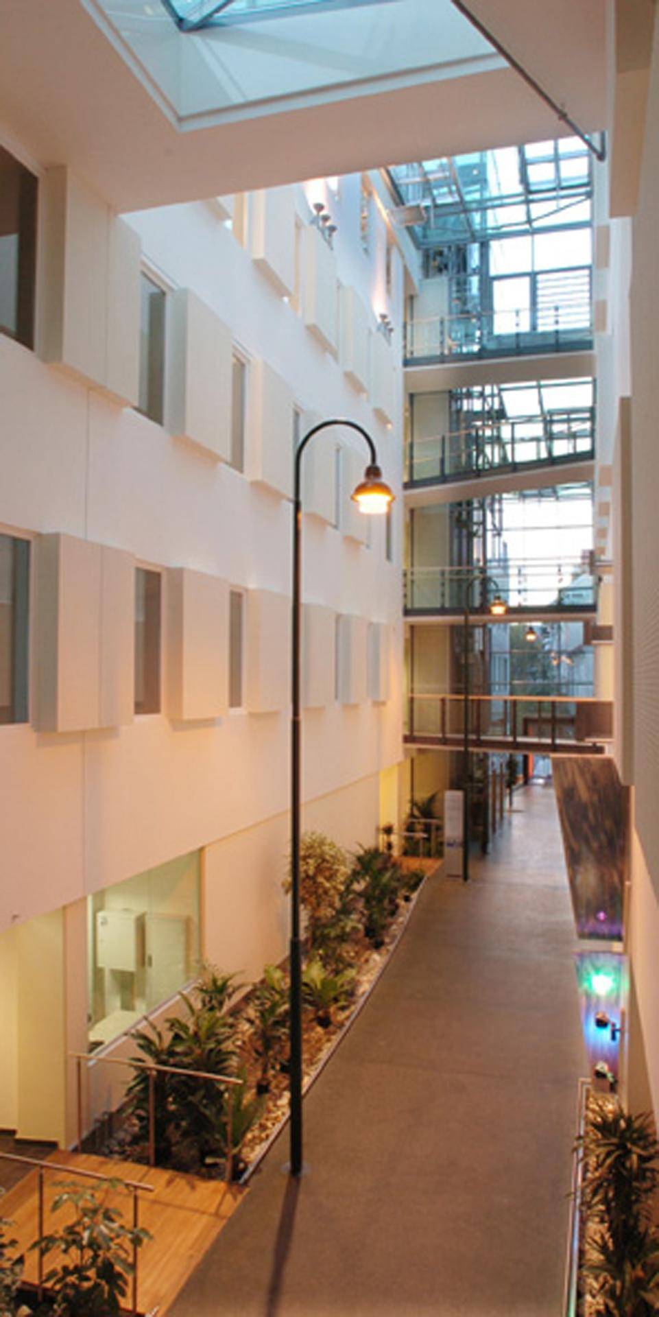 Innenansicht eines modernen Atriums mit Glasdach, Pflanzen und einer Straßenlaterne.