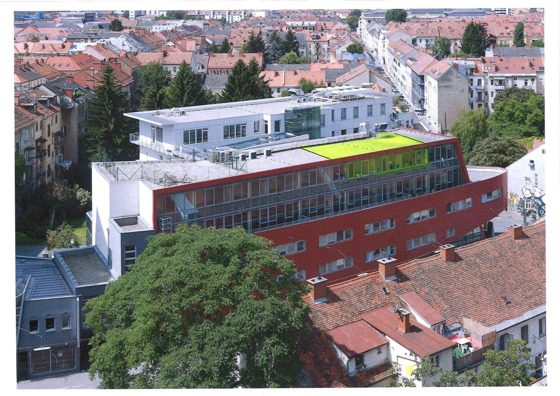 Luftaufnahme des modernen Gebäudes mit roter Fassade und grünen Dachelementen in städtischer Umgebung.