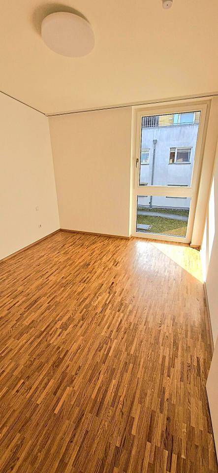 Unmöbliertes Schlafzimmer mit Parkettboden und großem Fenster zum Garten.