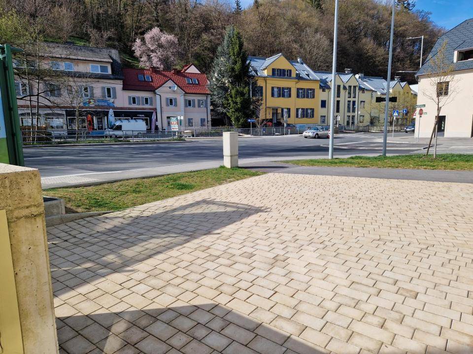 Blick auf die Straße mit bunten Gebäuden im Hintergrund und einem gepflasterten Vorplatz.
