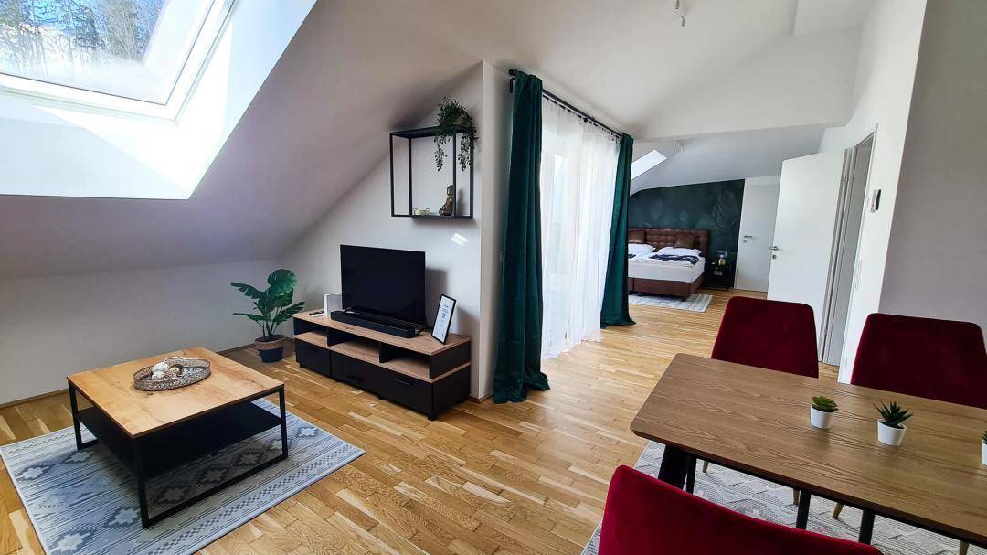 Heller Wohnbereich mit Dachschrägen, Holzboden und Blick ins Schlafzimmer.