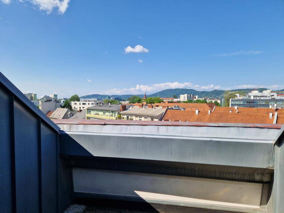 Weitblick über die Dächer der Stadt mit Bergen im Hintergrund unter einem klaren blauen Himmel.