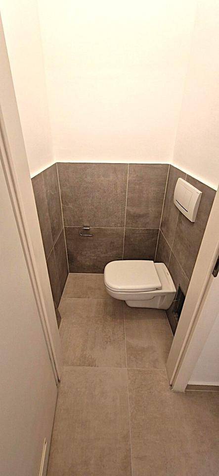 Modernes Gäste-WC mit wandhängender Toilette und grauen Fliesen an Wänden und Boden.
