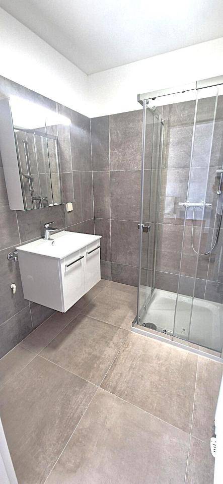 Modernes Badezimmer mit Duschkabine, Waschtisch und grauen Fliesen an Wänden und Boden.