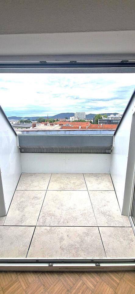 Kleiner Balkon mit Fliesenboden und Blick über die Dächer der Stadt und die umliegenden Berge.