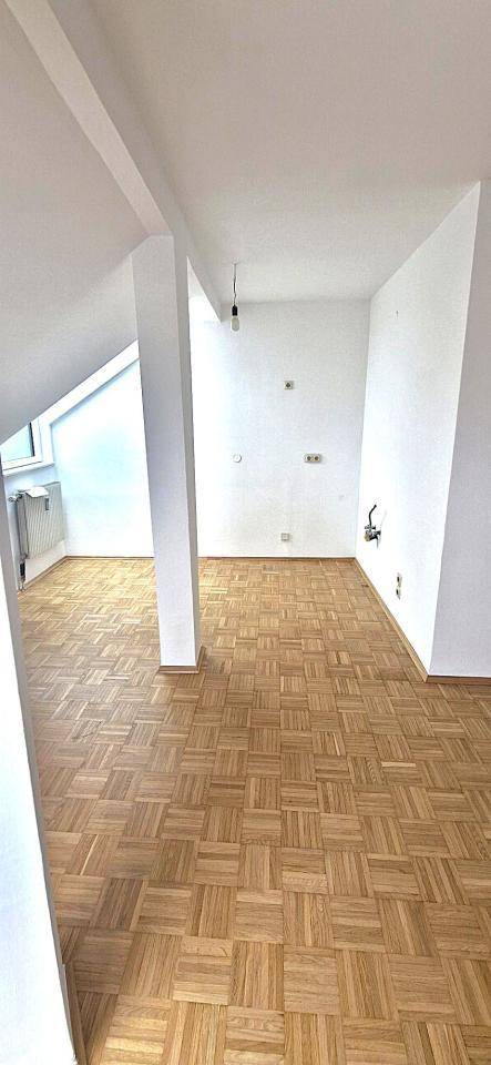 Heller Wohnbereich im Dachgeschoss mit Parkettboden, schrägen Wänden und Stützpfeilern.