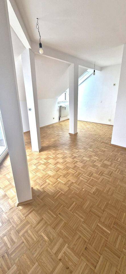 Geräumiger, heller Wohnbereich im Dachgeschoss mit Parkettboden, schrägen Wänden und Stützpfeilern.