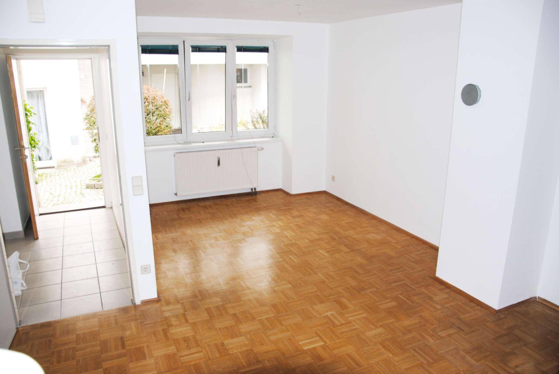Helles Wohnzimmer mit Parkettboden, weißen Wänden und Blick auf den Innenhof.