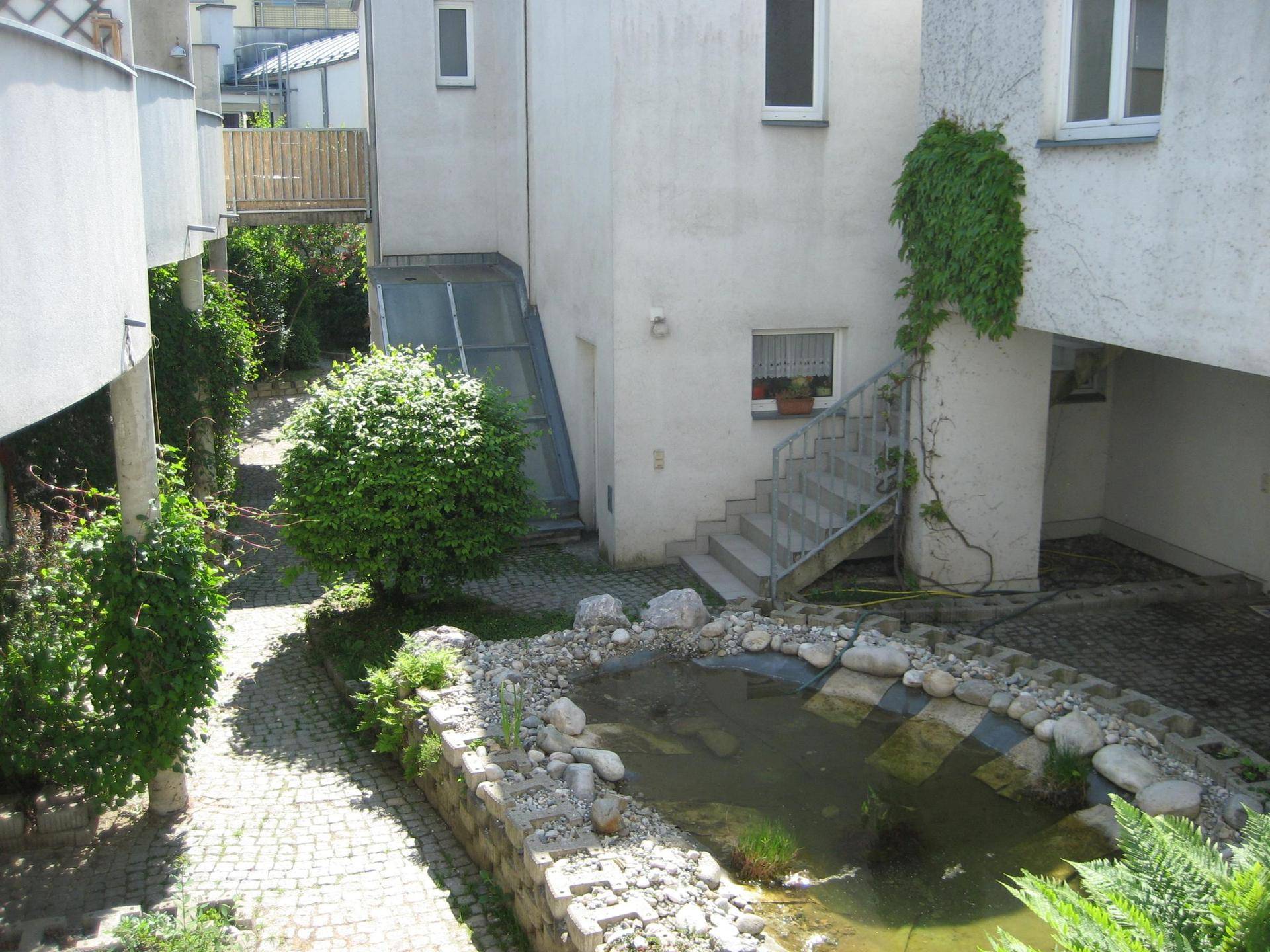 Außenbereich eines Wohnkomplexes mit einem kleinen Teich, gepflastertem Hof und viel Grün.