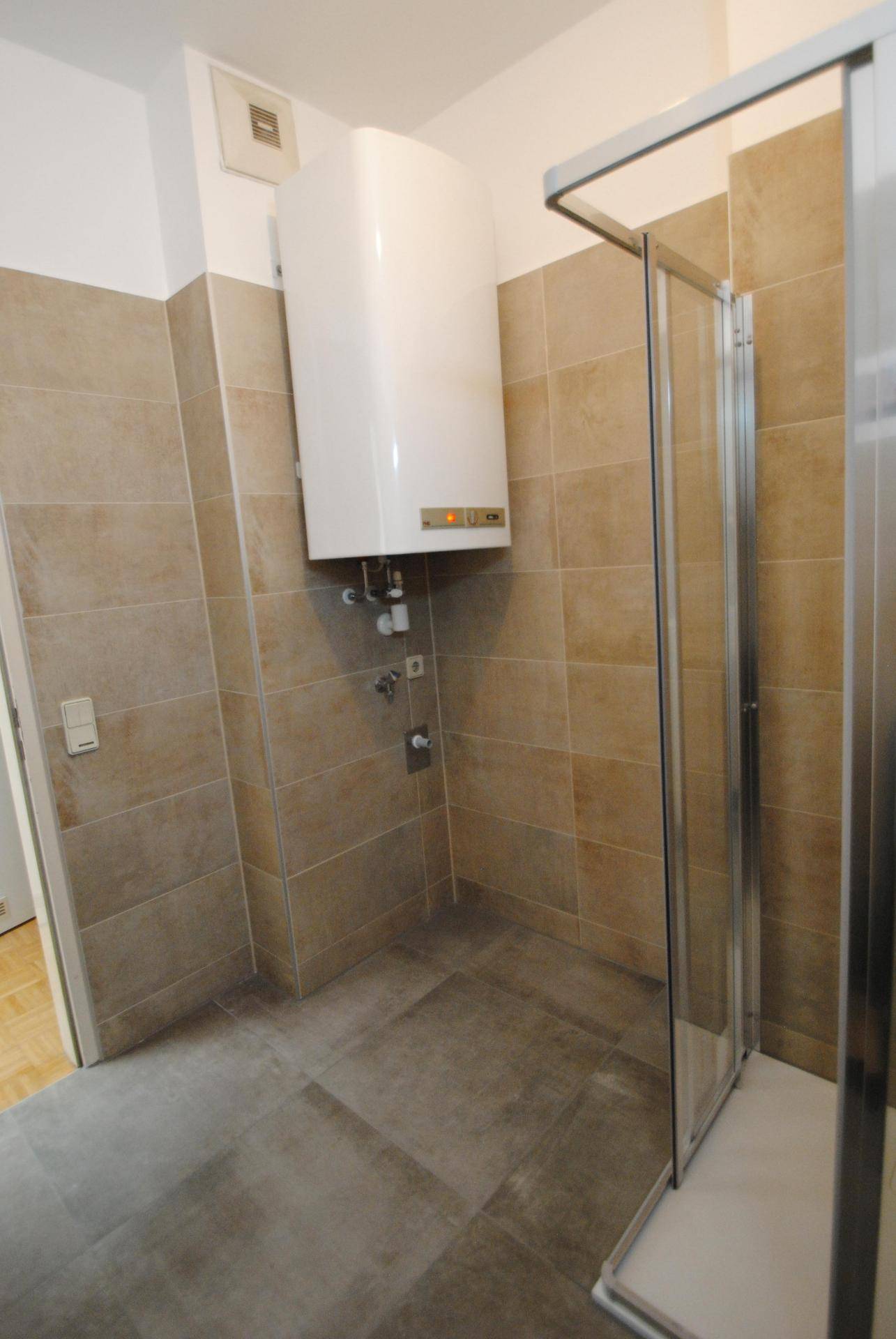 Badezimmer mit beigefarbenen Wandfliesen, grauen Bodenfliesen und einer Duschkabine.