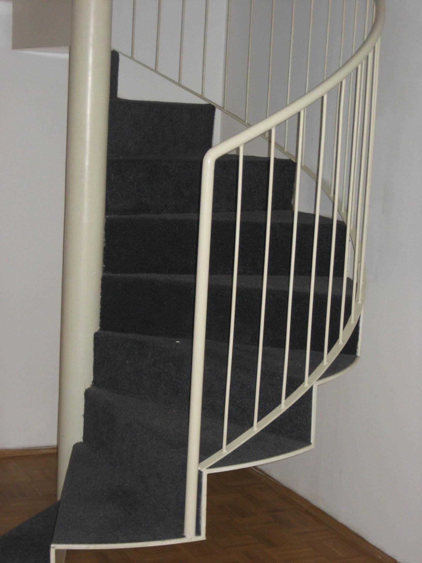 Detailansicht einer eleganten Wendeltreppe mit dunklem Teppichbelag und weißem Geländer.
