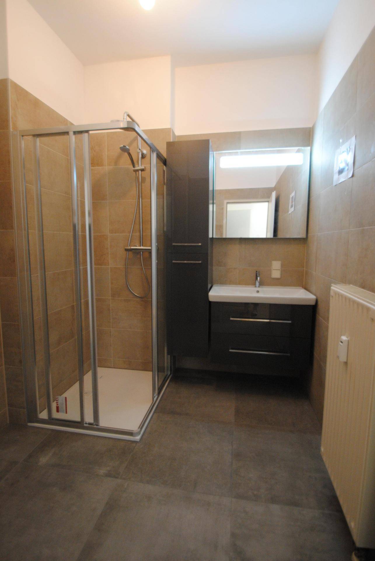 Modernes Badezimmer mit Duschkabine, Waschtisch mit Spiegel und Heizkörper.