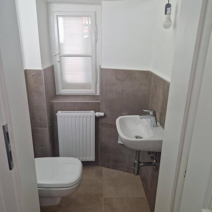 Modernes Gäste-WC mit Fenster, Wandfliesen und einem kleinen Waschbecken.