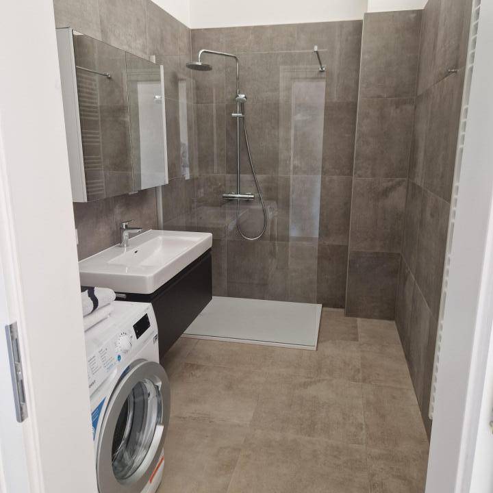 Modernes Badezimmer mit ebenerdiger Dusche, Waschmaschine und beheiztem Handtuchhalter.