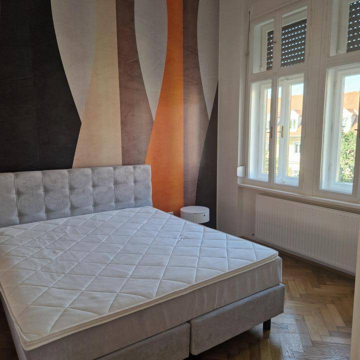 Helles Schlafzimmer mit großem Bett, Parkettboden und einem Fenster mit Blick nach draußen.