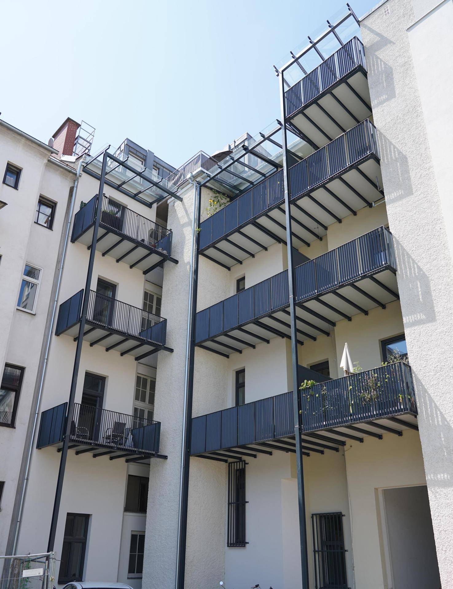 Rückfassade eines Gebäudes mit mehreren modernen Balkonen und Glasüberdachungen.