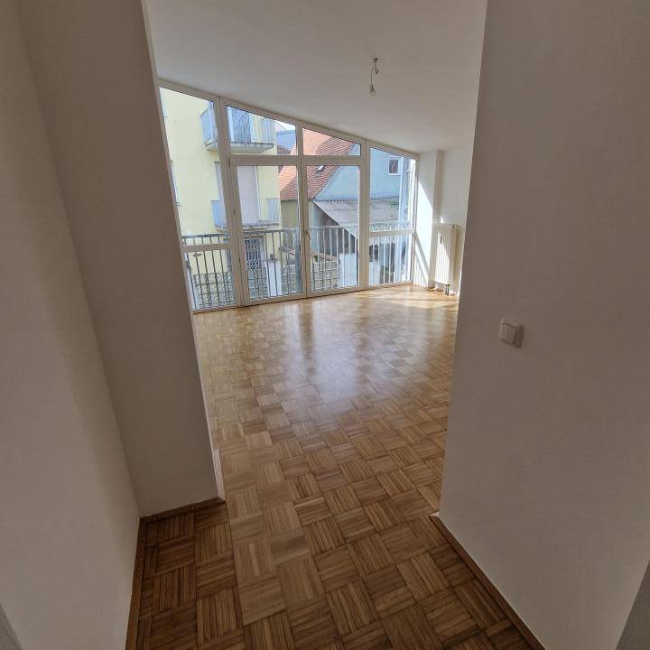 Heller Wohnraum mit Parkettboden und großen, schrägen Fenstern, die viel Tageslicht hereinlassen.