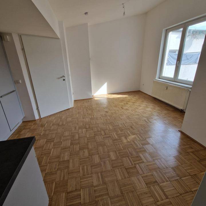 Heller Wohnbereich mit Parkettboden und Fenster, angrenzend an eine moderne Küchenzeile.