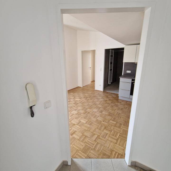 Blick vom Flur in den hellen Wohnbereich mit Parkettboden und angrenzender Küchenzeile.