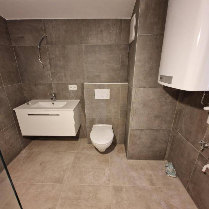 Zeitgemäßes Badezimmer mit schwebendem Waschtisch, Wand-WC und großformatigen grauen Fliesen.