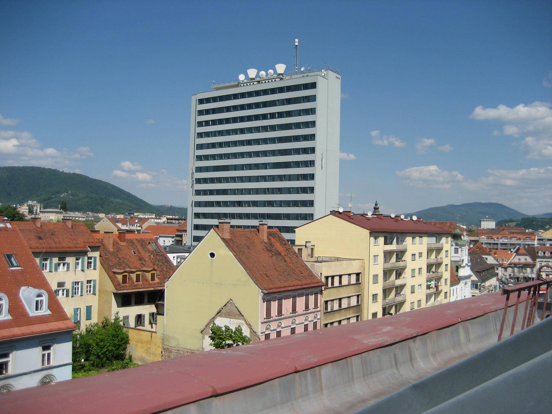 Weitblick über die Stadt mit einem markanten Hochhaus und weiteren Gebäuden unter einem klaren blauen Himmel.