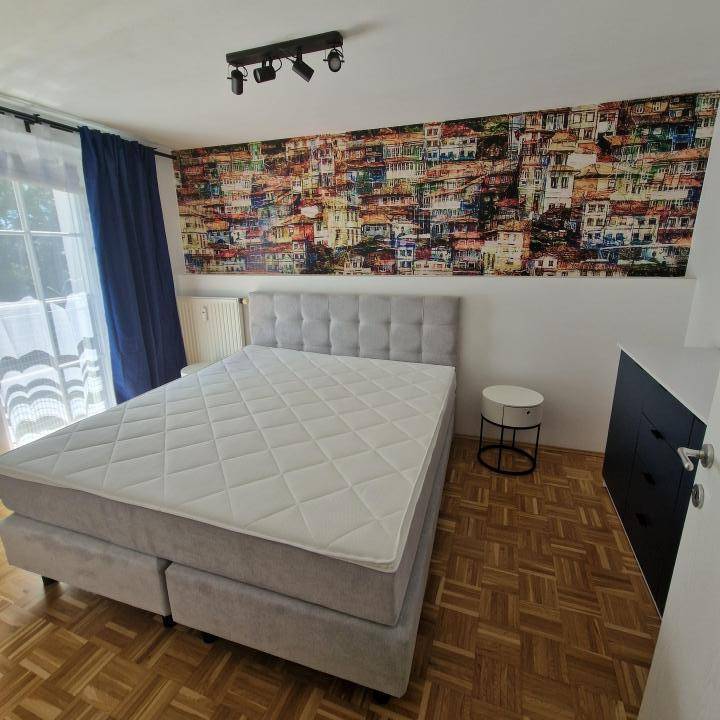 Schlafzimmer mit großem Bett, Parkettboden und einer farbenfrohen Wandtapete, die Akzente setzt.