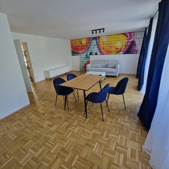 Geräumiger Wohn-Essbereich mit Parkettboden, moderner Einrichtung und auffälliger Wandmalerei als Blickfang.
