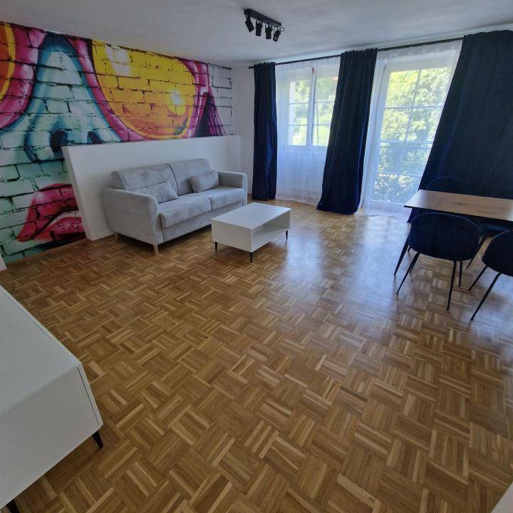 Heller Wohnbereich mit Parkettboden, Sofa und einem großen Fenster mit angenehmem Blick ins Grüne.