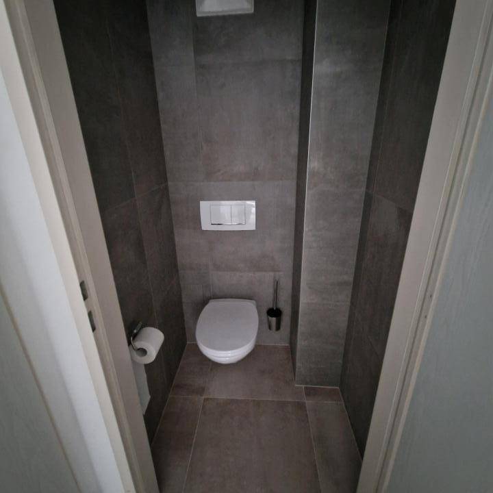 Separates WC mit modernen grauen Fliesen und einer wandhängenden Toilette für ein zeitgemäßes Ambiente.