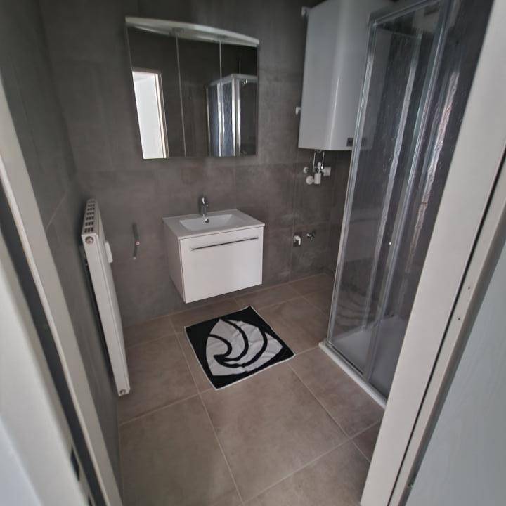 Modernes Badezimmer mit grauen Fliesen, Duschkabine und Waschtisch mit praktischem Spiegelschrank.