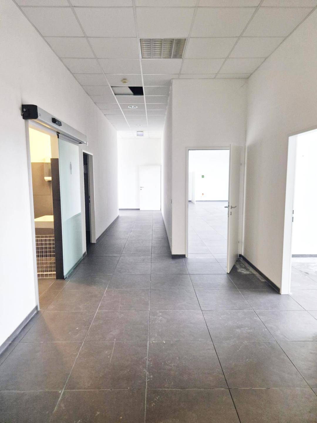 Heller Flur mit Fliesenboden und Zugang zu mehreren Büroräumen und Toiletten.