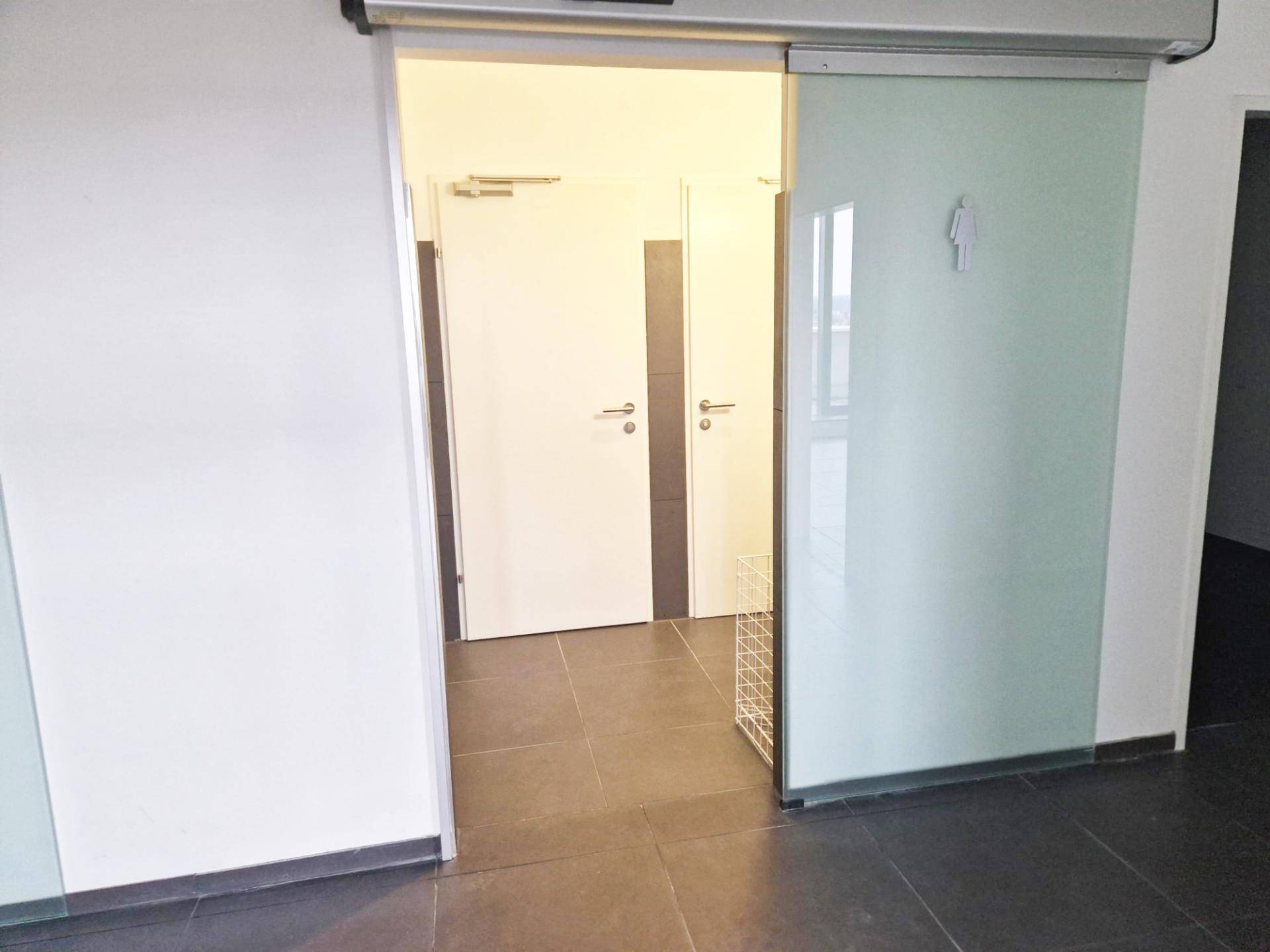 Eingangsbereich zu den Toiletten mit Schiebetür und Fliesenboden in einem modernen Design.
