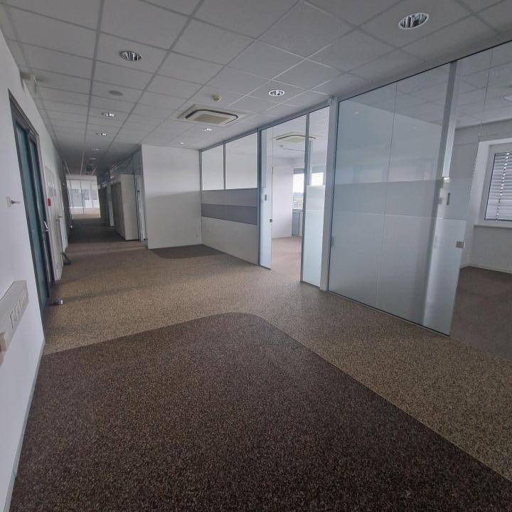 Langer Bürogang mit Teppichboden und Glaswänden, die zu den angrenzenden Büroräumen führen.