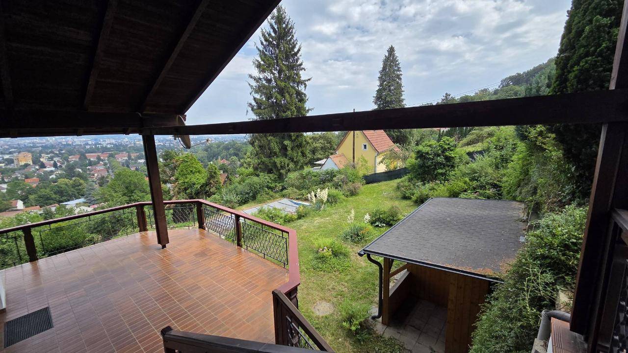 Große überdachte Terrasse mit Fliesenboden und weitem Blick über die Stadt und die grüne Umgebung.