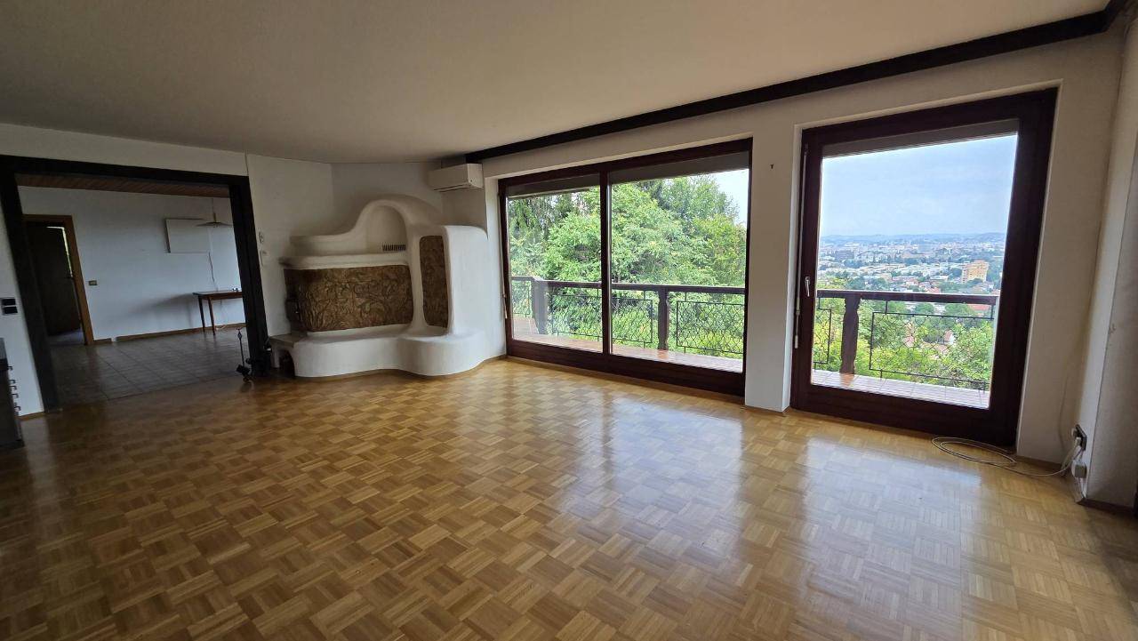 Helles Wohnzimmer mit Parkettboden, Kachelofen und großen Fenstern mit Panoramablick.