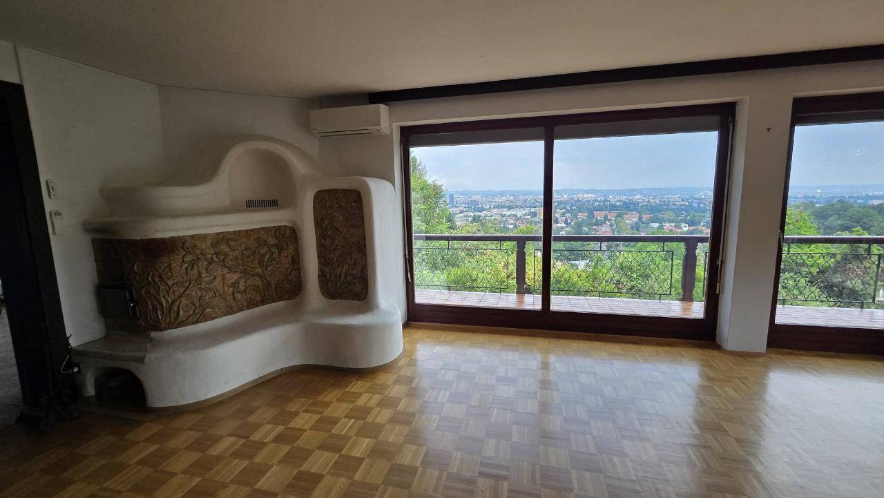 Geräumiges Wohnzimmer mit Holzboden, traditionellem Kachelofen und weitem Blick auf die Stadt.