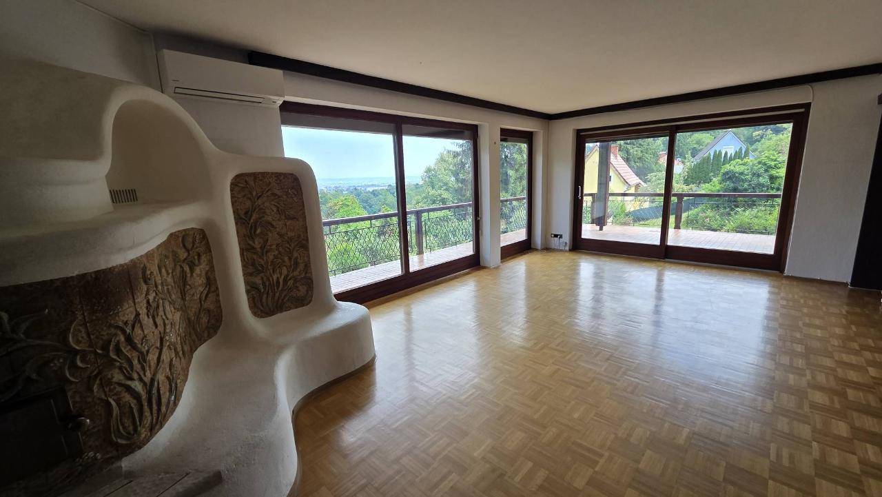 Geräumiges Wohnzimmer mit Parkettboden, Kachelofen und großen Fenstern mit Panoramablick.