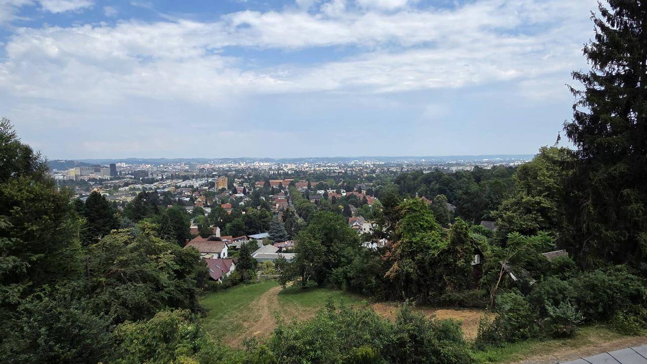 Weitläufiger Blick über eine grüne Landschaft mit verstreuten Häusern und einer Stadt in der Ferne.