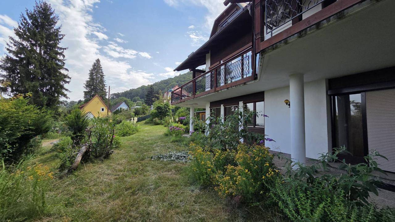 Seitenansicht des Hauses mit Balkon und einem weitläufigen Gartenbereich unter sonnigem Himmel.