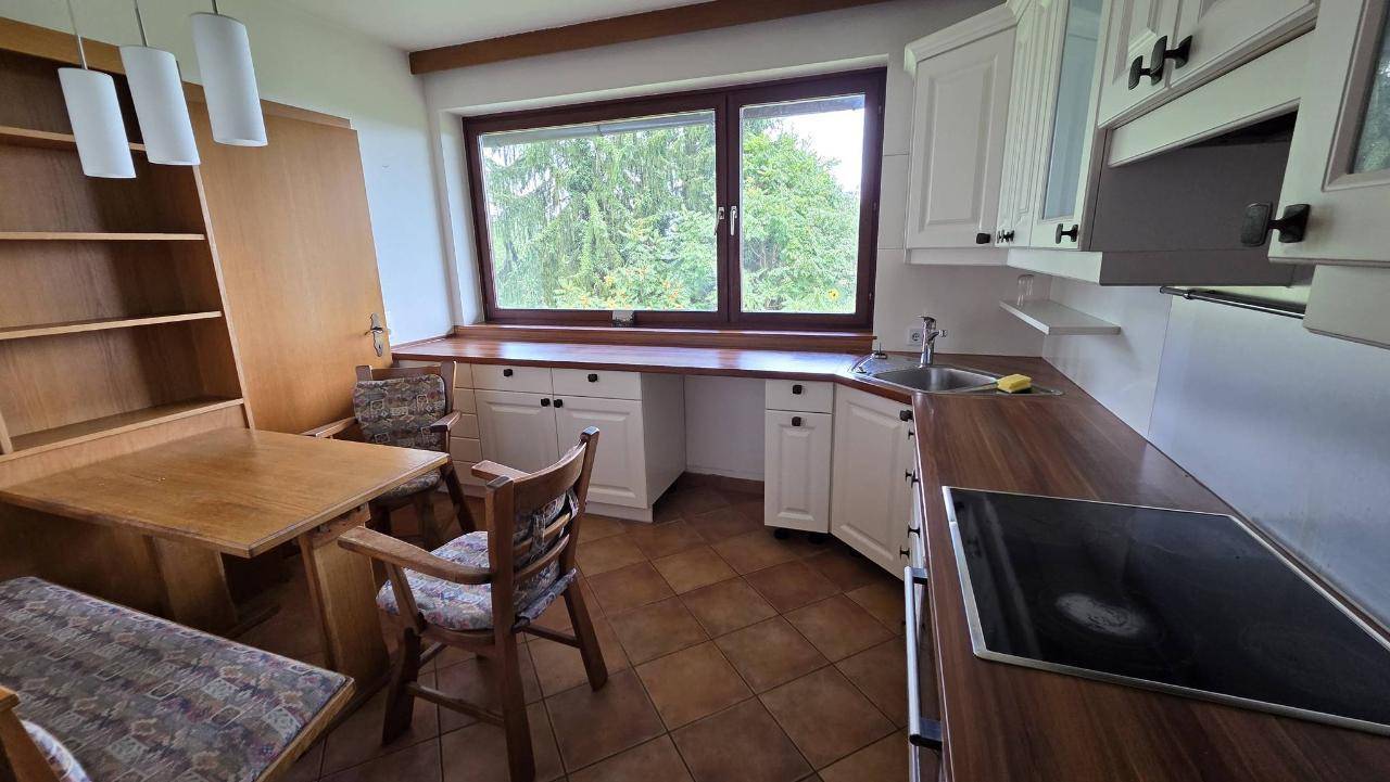 Funktionale Küche mit weißen Schränken, Holzarbeitsplatten und Essbereich am Fenster mit Blick ins Grüne.