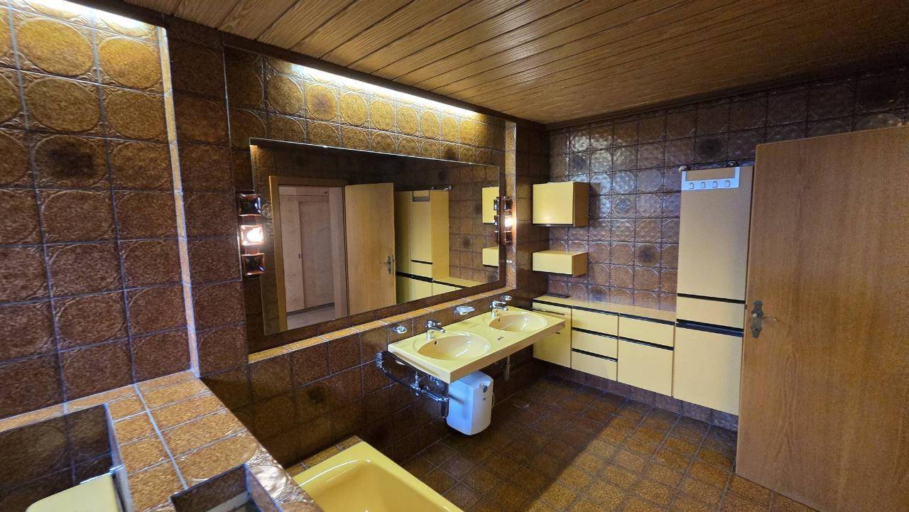Retro-Badezimmer mit braunen Fliesen, gelben Armaturen und großem Spiegel über dem Doppelwaschbecken.