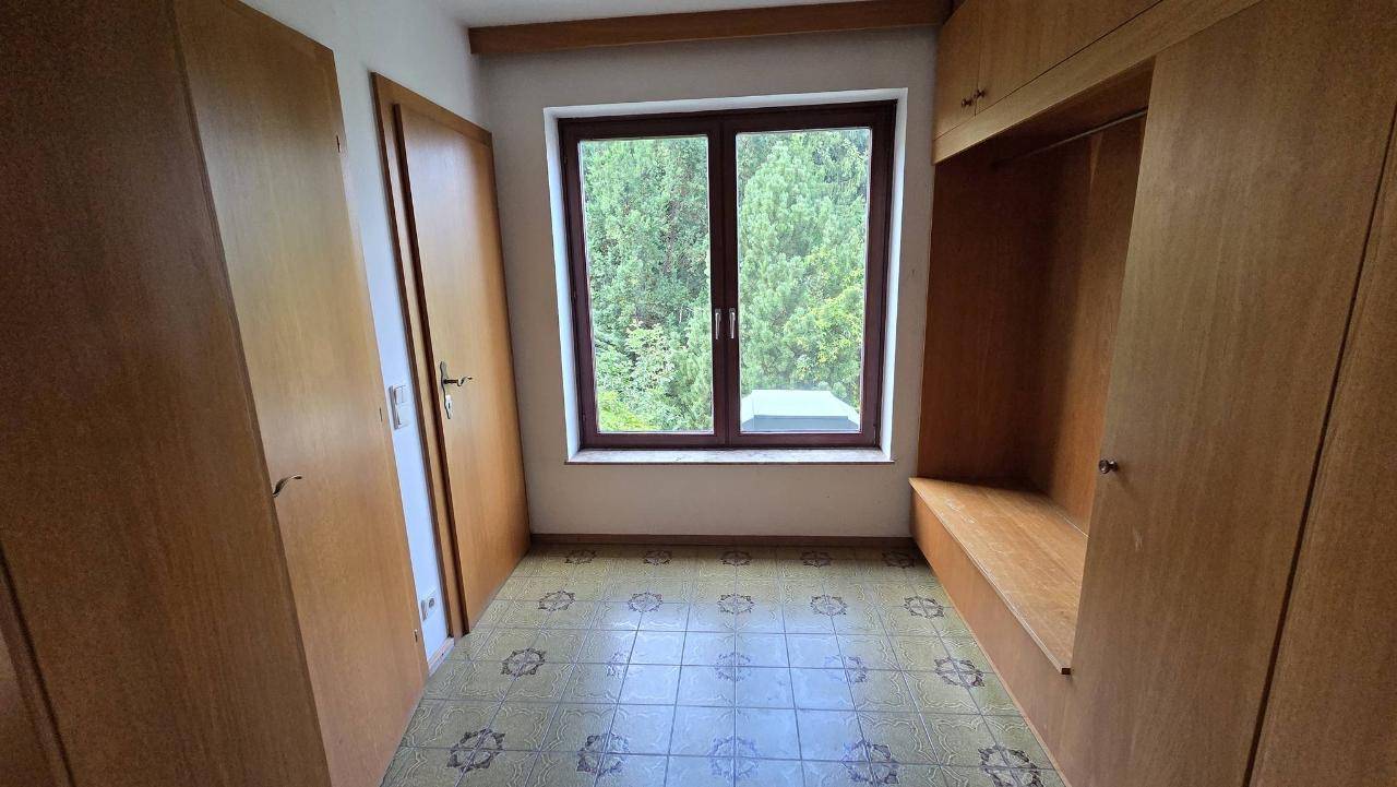 Kleines Zimmer mit Einbauschränken, Fenster mit Blick ins Grüne und gemustertem Bodenbelag.